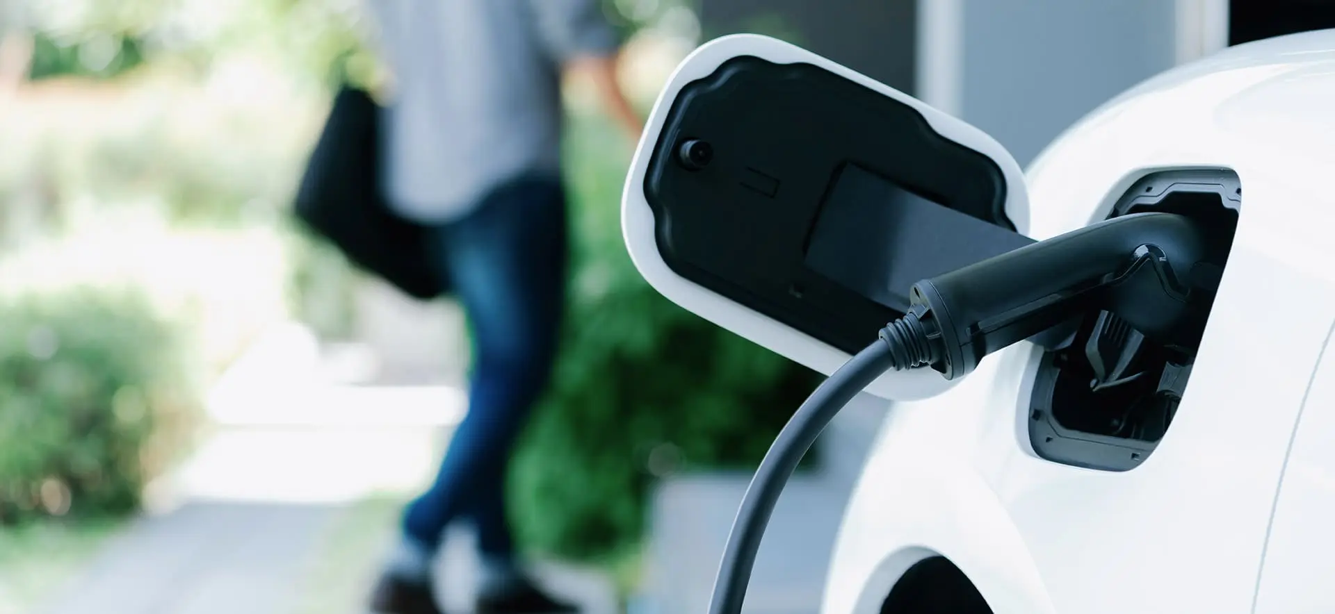 Voiture électrique en train de charger à la station de recharge de la maison avec un homme progressif flou marchant à l'arrière-plan.