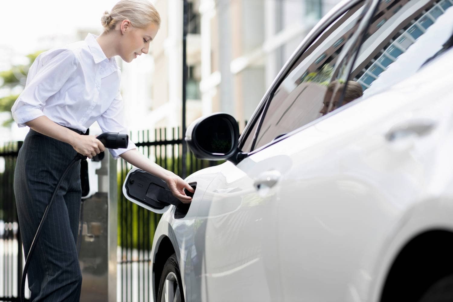 Femme qui branche son véhicule électrique directement sur sa borne de recharge résidentielle